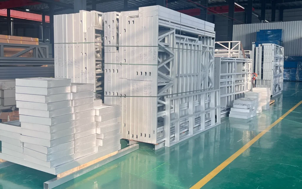 Bundled light-gauge steel wall frames and stacked components in a factory workshop.